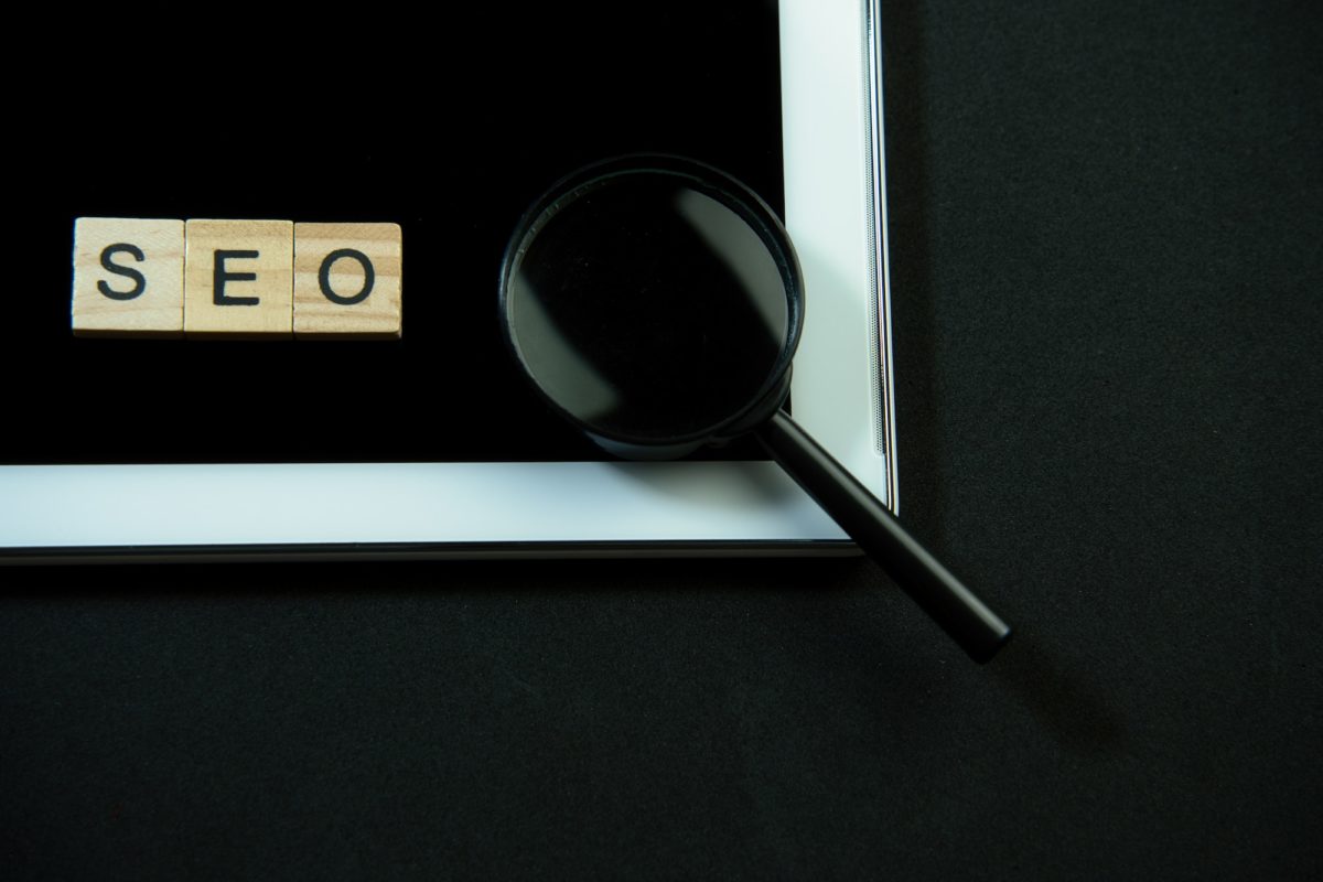 SEO written in wooden letters, tablet and a magnifying glass.